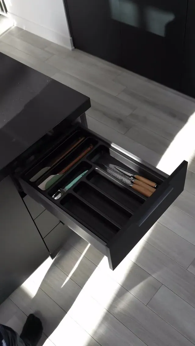 Aperçu d’un tiroir de cuisine avec des couverts et des ustensiles rangés dans un séparateur noir.
